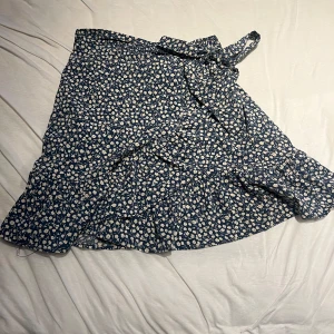 Blommig omlottkjol från ONLY - Säljer en superfin blå omlottkjol från ONLY med sött blommönster. Kjolen har volangdetaljer och ett knytband i midjan för perfekt passform. Perfekt för vår och sommar! 🌸
