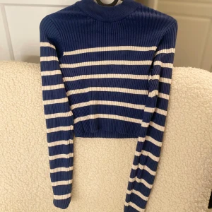 Randig ribbad croppad tröja - Säljer en snygg randig ribbad croppad tröja med långa ärmar. Perfekt för en stilren look. Finns i två färgkombinationer: blå och beige samt beige och svart.