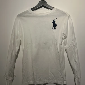 Vit långärmad tröja från Ralph Lauren - Säljer en stilren vit långärmad tröja från Ralph Lauren med det klassiska polospelarlogotypen på bröstet och en stor siffra 3 på ryggen. Perfekt för en avslappnad och sportig look. Passar bra till jeans eller chinos. Passar alla runt 150 till 158. Tröjan är oanvänd 
