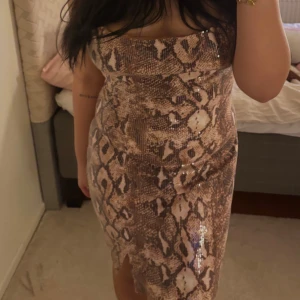 Ormmönstrad paljettklänning - Snygg ormmönstrad klänning med paljetter som ger en glittrig effekt. Klänningen  har en slits framtill. Perfekt för en kväll ute! Också helt ny och är oanvänd!!