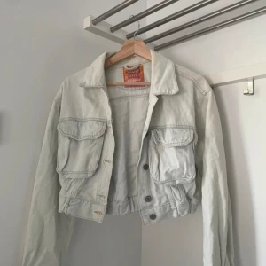 Croppad jeansjacka från Pull&Bear Sadie Sink - Säljer en croppad jeansjacka från Pull&Bear med långa ärmar och stora fickor framtill. Jackan har en klassisk krage och knappar för stängning. Perfekt för en avslappnad stil. Från Sadie Sinks kollektion.