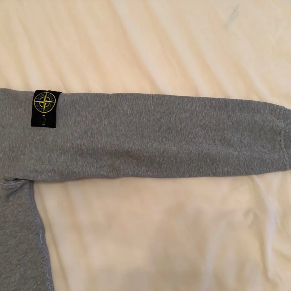 Säljer en stilren grå tröja från Stone Island med deras ikoniska märke på ärmen. Tröjan har en rund hals och långa ärmar, perfekt för en avslappnad look. Passar bra till både jeans och chinos. Använt den 4 gånger. Neuletakit & Villapaidat.