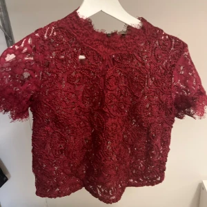 Vinröd spetsblus - Säljer en vinröd spetsblus med korta ärmar. Blusen har ett fint mönster och är perfekt för vardag å fest.