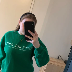 Grön sweatshirt  - Säljer en grön sweatshirt med vit text på framsidan. Tröjan har långa ärmar och en avslappnad passform. Använd endast en gång så den är i mycket bra skick.