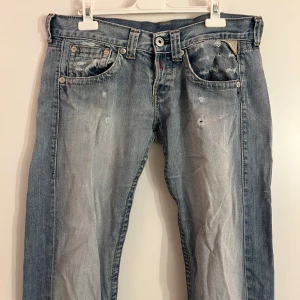 Blå jeans  - Säljer ett par blå jeans med coola slitningar och en unik broderad detalj på baksidan. De är väldigt lågmidjade, har en rak passform och en vintage/ y2k stil. De har några större slitningar som visas på bild 4 & 5. Super snygga!