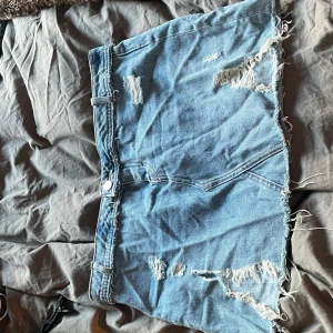 Blå jeanskjol med slitningar - Säljer en supersnygg blå jeanskjol med slitningar. Har sytt om den till lågmidjad! Passar perfekt för sommaren 