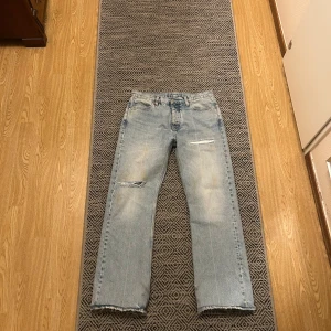 Hope Relaxed Bootcut Jeans - Säljer ett par ljusblå jeans med slitningar på knäna och råa kanter. De har en straight passform och är högmidjade, vilket ger en avslappnad look. Perfekta för en casual stil. Dessa är uppsydda cirka 2 centimeter så det är en size 30/30