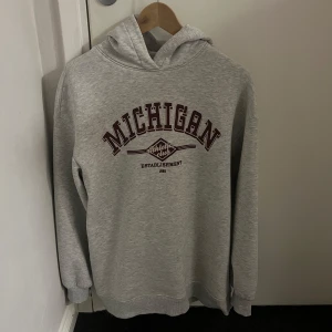 Grå hoodie med Michigan-tryck - Säljer en grå hoodie med tryck av 'Michigan' i vinrött på framsidan.