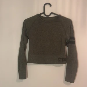 Grön träningsset från Stronger - Säljer ett Grönt träningsset från Stronger i storlek XS. Setet består av en långärmad topp och matchande leggings, båda med svarta ränder och textdetaljer. Perfekt för träning och bekvämt att bära.