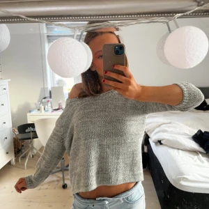 Grå stickad offshoulder tröja - Säljer en snygg grå stickad tröja med offshoulder-design. Tröjan är croppad och har långa ärmar, perfekt för en avslappnad stil. Passar bra till jeans och har en jättefin öppen rygg
