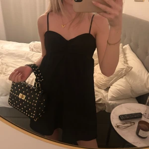 Svart klänning med smala axelband - Snygg svart klänning med smala axelband och en enkel design. Perfekt för en stilren look. Klänningen har en kort längd och en lätt v-ringad detalj framtill.