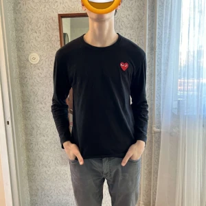 Svart långärmad cdg tröja - Säljer en stilren svart cdg långärmad tröja med ett rött hjärta på bröstet. Perfekt för en avslappnad look. Tröjan har en normal passform och är tillverkad i ett mjukt material.