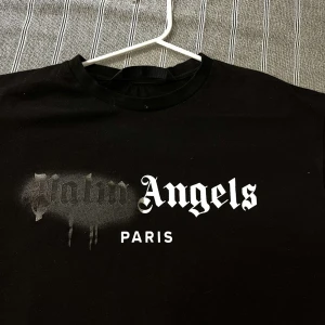 Svart t-shirt från Palm Angels - Snygg svart t-shirt från Palm Angels med tryck i vitt och grått på framsidan. Perfekt för en stilren och modern look. T-shirten har en klassisk passform och rund hals.