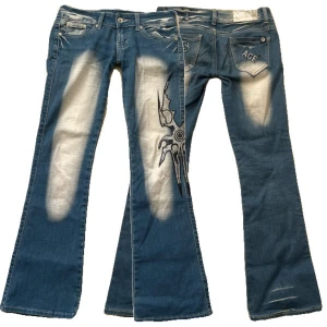 Blå jeans med tryck från Crazy Age - Snygga blå jeans från Crazy Age med unikt tryck på benen och slitna detaljer. Byxorna har en bootcut-stil och är dekorerade med paljetter. Perfekta för dig som vill sticka ut med en cool look.