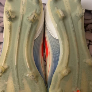 Adidas F50 fotbollsskor - Snygga Adidas F50 fotbollsskor i vitt med blå och röda detaljer. Skorna har en strömlinjeformad design med dobbar för optimalt grepp på planen. Perfekta för den som vill ha stil och prestanda i ett. Använd i 4måndader 