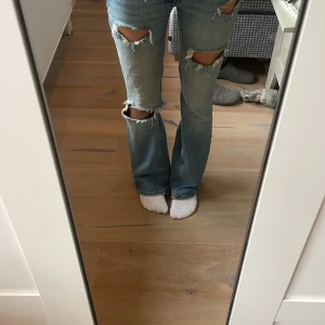 Blå bootcut jeans med slitningar - Snygga blå bootcut jeans med slitningar på knäna och låren. Det står att det är strl 32 men jag skulle säga att dom är mindre(Köparen står för frakt)