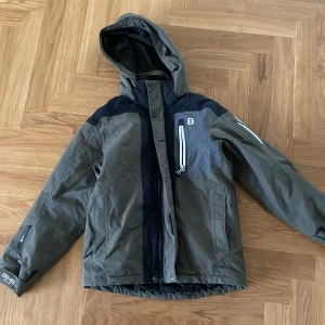 Grön och svart jacka från 8848 Altitude - Säljer en grön och svart jacka från 8848 Altitude. Jackan har en avtagbar huva och dragkedja framtill. Perfekt för skidbacken med sin stilrena design och praktiska fickor. 