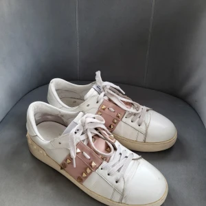 Valentino Rockstud sneakers, strl 40 - Snygga Valentino Rockstud sneakers i vitt med rosa detaljer och ikoniska nitar. Skorna har snörning och en bekväm passform. Perfekta för att ge din outfit en lyxig touch.