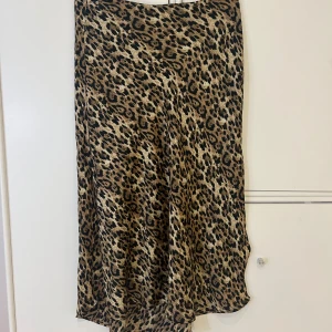 Leopardmönstrad kjol - Säljer en supercool leopardmönstrad kjol i mycket bra skick. Helt oanvänd. Den är perfekt för både vardag och fest! Kjolen har en normal passform och är gjord i ett lätt och bekvämt material. Den är enkel att matcha med en enkel topp eller en snygg blus för en mer uppklädd look. Det är ”slitsar” på sidorna. 