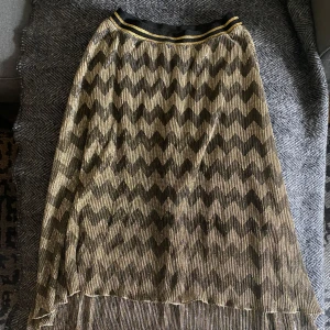 Mönstrad kjol från Rue de Femme - Säljer en superfin kjol från Rue de Femme i storlek S men är som M. Den har ett coolt zigzag-mönster i svart och guld, perfekt för både vardag och fest. Kjolen är i nyskick och har en elastisk midja för bästa passform. 