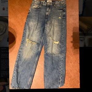 Blå jeans från Pull&Bear - Säljer ett par snygga blå jeans från Pull&Bear i storlek EUR 42. De har en cool slitning på knäna för en avslappnad look. Perfekta för en casual outfit!  Storlek 32-34