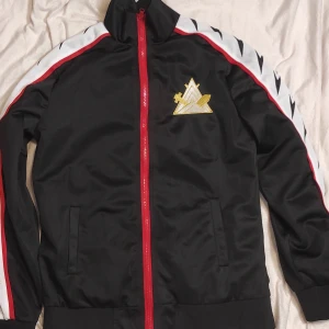 Rins captian jacket cosplay from free iwatobi swimclub - Säljer en svart träningsjacka med röd dragkedja och coola vita och svarta detaljer på ärmarna. Den har ett guldtryck på bröstet och stora guldtecken på ryggen. Perfekt för sport eller chill dagar. Passar bra till både träning och vardag! Detta tillhör en cosplay men kan användas vanligt också pga hur bekväm den är!