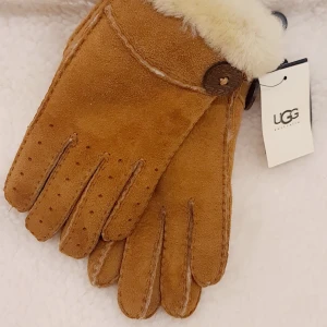 Bruna handskar från UGG - Säljer ett par snygga bruna handskar från UGG i storlek M. De är gjorda av äkta fårskinn och har en mjuk, fluffig kant. Perfekta för att hålla händerna varma under kalla vinterdagar. De är i nytt skick och kommer med originaletikett.