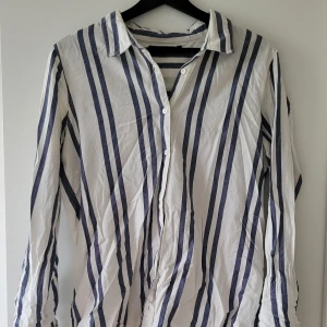 Randig skjorta från BikBok - Säljer en snygg randig skjorta från BikBok i storlek S. Skjortan är vit med blå ränder och har långa ärmar. Den har en klassisk krage och knappar framtill. Använd endast 1 gång. Storlek: S  Skickas inslagen i silkespapper i vattentätt paket.   Skicka pm för fler bilder. 