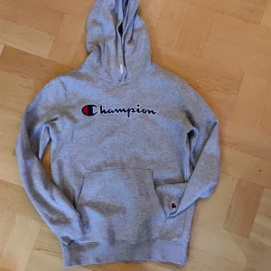 Grå hoodie från Champion - Säljer en grå hoodie från Champion i mycket bra skick. Den har en stor Champion-logga på framsidan och en praktisk magficka. Perfekt för höst och vinter, och den är supermjuk och bekväm. Passar både till vardags och chillkvällar. 🩶