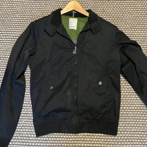 J.Lindeberg Vår Jacka - Säljer en snygg svart jacka från J.Lindeberg i mycket bra skick och storlek M . Jackan har en dragkedja framtill och två knappar vid fickorna. Perfekt för höst och vår.