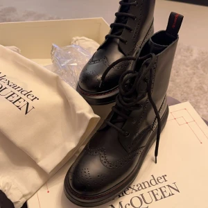 Svarta boots från Alexander McQueen - Säljer ett par svarta boots från Alexander McQueen i nytt skick. De är tillverkade i skinn med snygg snörning och brogue-detaljer. Perfekta för höst och vinter med en robust sula för extra grepp. Kommer med extra skosnören och originalförpackning.
