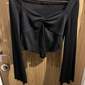 Svart långärmad topp med knyt - Snygg svart långärmad topp med knyt framtill. Perfekt för en kväll ute eller en avslappnad dag. Den har en croppad stil som ger en modern look. Materialet känns mjukt och bekvämt.