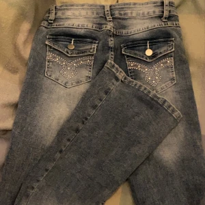Blå jeans med broderade bakfickor - Säljer ett par snygga blå jeans med broderade detaljer på bakfickorna och en bekväm passform. Kan enkelt matchas med olika toppar. Skicka ett meddelande vid intresse!