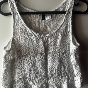 Vit spetslinne från H&M - Säljer ett superfint vitt spetslinne från H&M i storlek S. Perfekt för sommardagar eller som ett lager under en kavaj. Linnet är ärmlöst och har en vacker spetsdesign som ger en romantisk touch. Passar både till vardags och fest!
