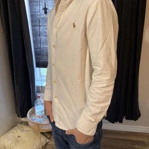 Vit skjorta från Ralph Lauren - Säljer en klassisk vit skjorta från Ralph Lauren i storlek 16. Den har en broderad logga på bröstet som ger en stilren touch. Perfekt för både vardag och fest! 🕺