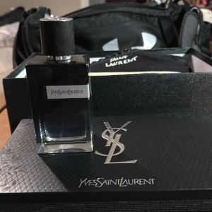 Yves Saint Laurent parfym - Säljer en elegant parfym från Yves Saint Laurent. Flaskan är stilren och fyrkantig med en mörk tonad glasdesign och ett svart lock. Perfekt för den som vill ha en sofistikerad doft som passar både dag och natt. Kommer i originalförpackning.