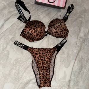 Leopardmönstrad bh och trosa från Victoria's Secret - Snyggt set med leopardmönstrad bh och matchande trosa från Victoria's Secret. Bh:n har vadderade kupor och justerbara axelband med logotyp. Nytt skick. Trosorna är i storlek M.