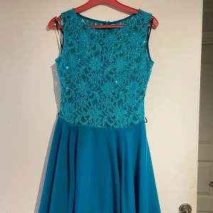 Turkos klänning med spetsdetaljer - Säljer en superfin turkos klänning med spetsdetaljer på överdelen. Den är ärmlös och har en elegant, flödande kjol. Perfekt för sommarens fester eller en speciell kväll. Klänningen är i mycket bra skick och ger en fräsch och stilren look.