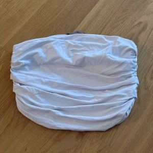 Vit tubtopp - Säljer en stilren vit tubtopp i mjukt material. Perfekt för sommardagar eller som en bas i din festoutfit. Toppen har en enkel design med rynkade detaljer som ger en snygg passform. Passar bra till både jeans och kjol!