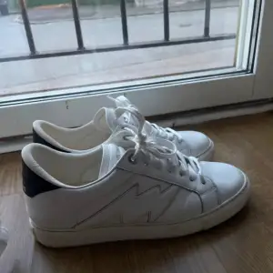 Säljer ett par vita sneakers från Zadig & Voltaire i bra skick. De har en snygg svart detalj på hälen och klassisk snörning. Perfekta för både vardag och fest! Storlek är inte angiven, men de ser ut att vara i normal passform.