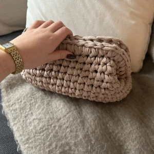 Beige virkad clutchbag - Säljer en superfin beige virkad clutchbag som är perfekt för att bära med sig det viktigaste. Den är handgjord och har en mysig, bohemisk stil. Perfekt som handväska eller necessär🧶