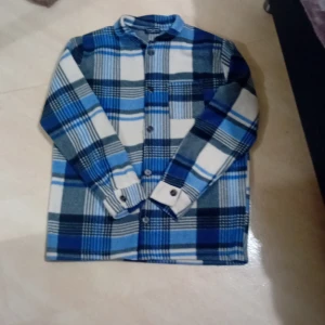 Rutig overshirt från Copacabana - Säljer en snygg rutig overshirt från Copacabana i blå, vit och svart. Perfekt för höst och vinter med sitt mjuka och varma material. Skjortan har långa ärmar och knappar framtill. Perfekt för en avslappnad stil eller lager på lager-look. 🧥Den är xl men den är mindre i storlek