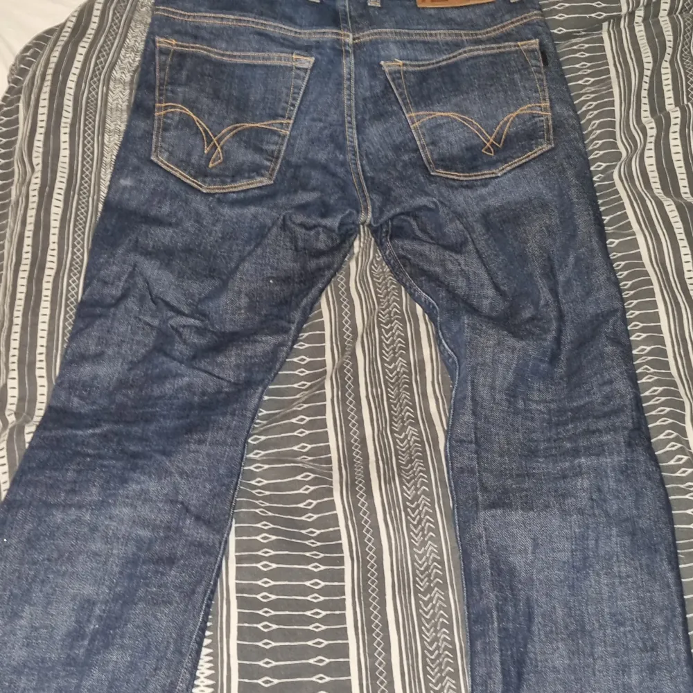 Säljer ett par klassiska blå jeans i bra skick. De har en straight passform och är tillverkade i slitstarkt denim. Jeansen har en knappgylf och snygga detaljer på bakfickorna. Perfekta för både vardag och fest!. Jeans & Byxor.