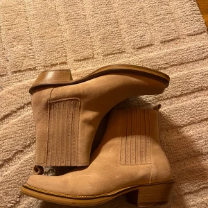 J Lindeberg James square toe boot  - Säljer ett par snygga beige j Lindeberg boots i mocka. De har en klassisk design med elastiska paneler på sidorna och en låg klack. Perfekta för både höst och vår. Skorna är i helt nya och kommer i originalkartong. Nypris 3600, storlek 43