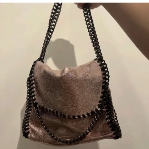 Glittrig axelväska med kedjedetaljer - Säljer en superfin glittrig axelväska i en skimrande brun nyans. Väskan har coola kedjedetaljer som ger den en edgy look. Perfekt för en utekväll eller fest! 👜✨