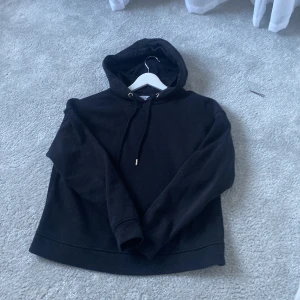 Svart hoodie från Lindex - Säljer en svart hoodie från Lindex i storlek XS. Den är supermjuk och perfekt för både mysiga hemmakvällar och chill dagar ute. Hoodien har en klassisk design med dragsko i huvan och långa ärmar. Perfekt basplagg för garderoben!