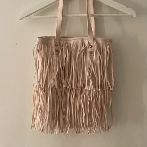 Väska - Säljer denna fina väskan med fransar då den inte används längre! Väskan är gjord i syntetmaterial och har en dragkedja inuti! Lite små defekter men annars bra skick!🤍💕