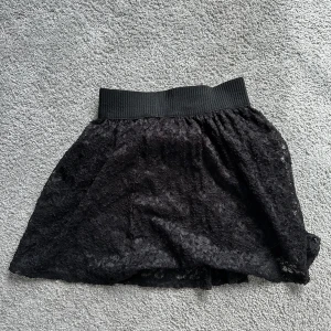 Svart spetskjol från Gina Tricot - Säljer en superfin svart spetskjol från Gina Tricot. Kjolen har en elastisk midja för extra komfort och är perfekt för både vardag och fest. Den är i storlek S och har en vacker spetsdetalj som ger en elegant touch. Passar perfekt till en enkel topp eller en snygg blus!