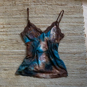 Mönstrad linne med spetsdetaljer - Säljer en superfin linne med ett unikt mönster i blått och brunt. Den har tunna axelband och vackra spetsdetaljer i brunt med små pärlor. Perfekt för sommardagar eller som ett lager under en kofta.