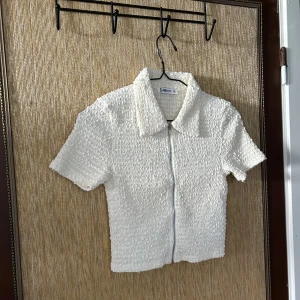 Vit kortärmad topp med dragkedja från Zara - Säljer en snygg vit kortärmad topp. Den har en unik textur och en dragkedja framtill. Perfekt för både vardag och fest! 🖤